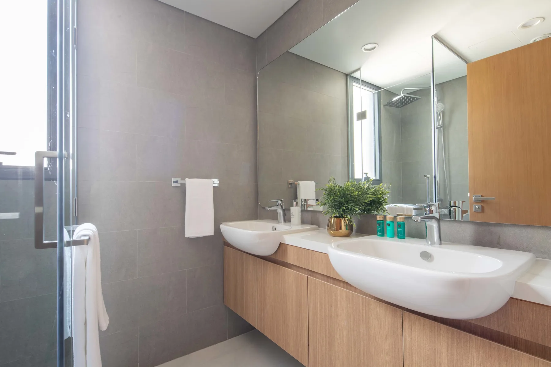 Un baño moderno con lavabos dobles, un espejo amplio y una ducha de vidrio.