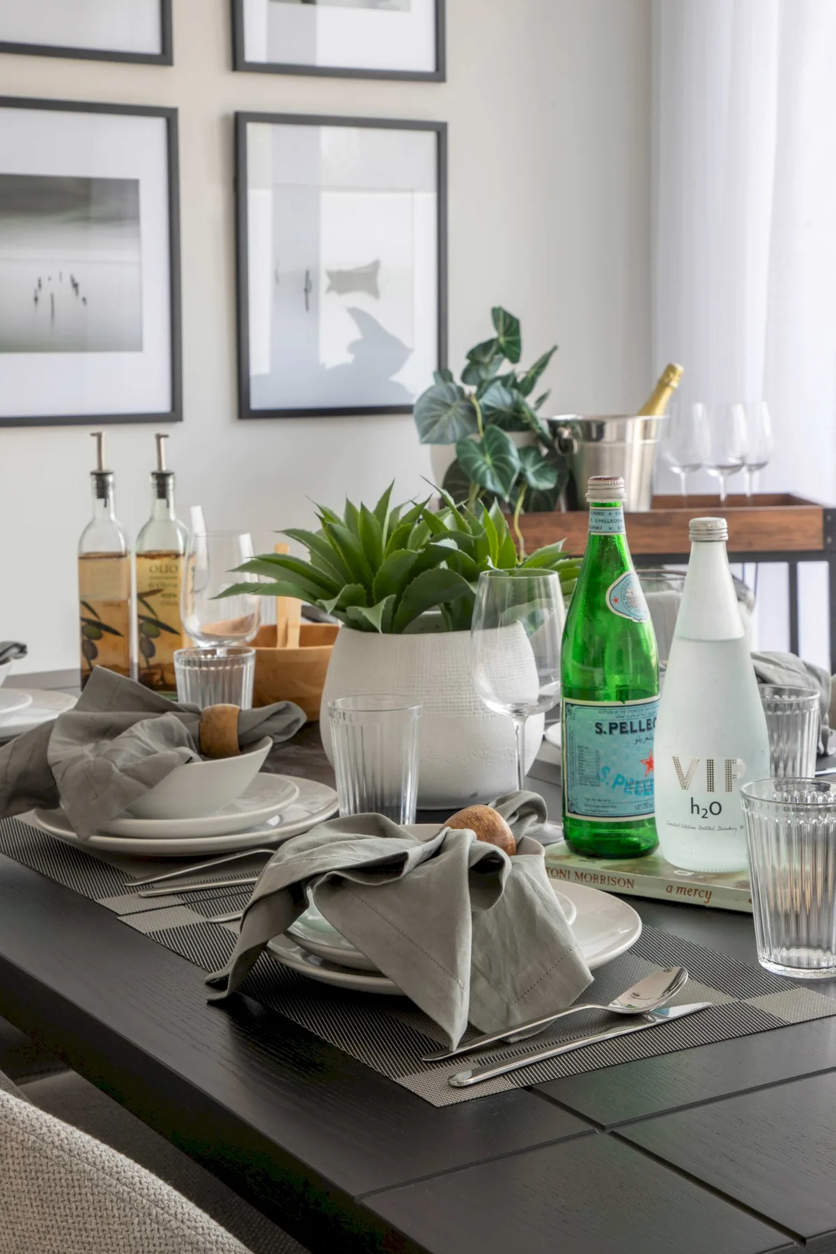 Una mesa de comedor está preparada con platos, vasos, botellas y una planta en maceta.