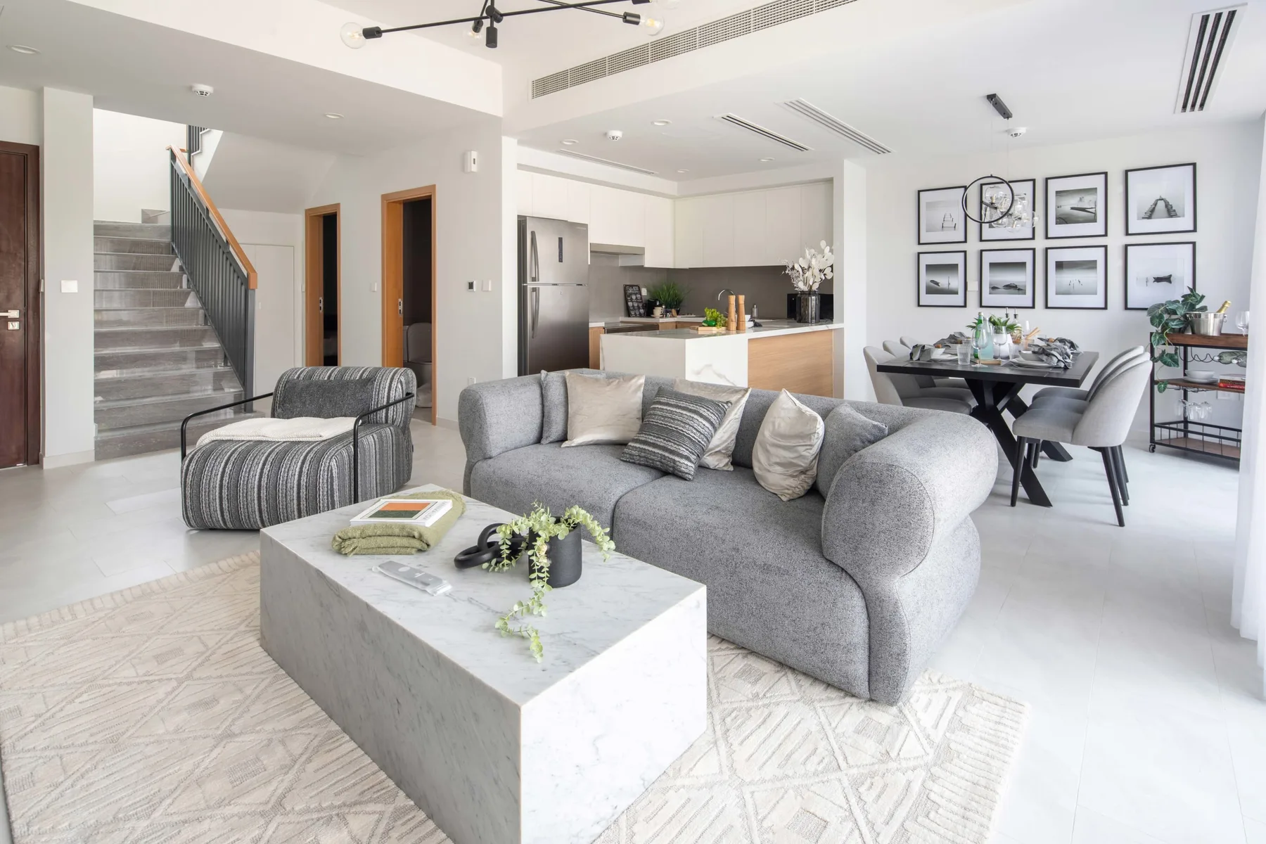 Una sala luminosa con asientos grises y una cocina y comedor abiertos.