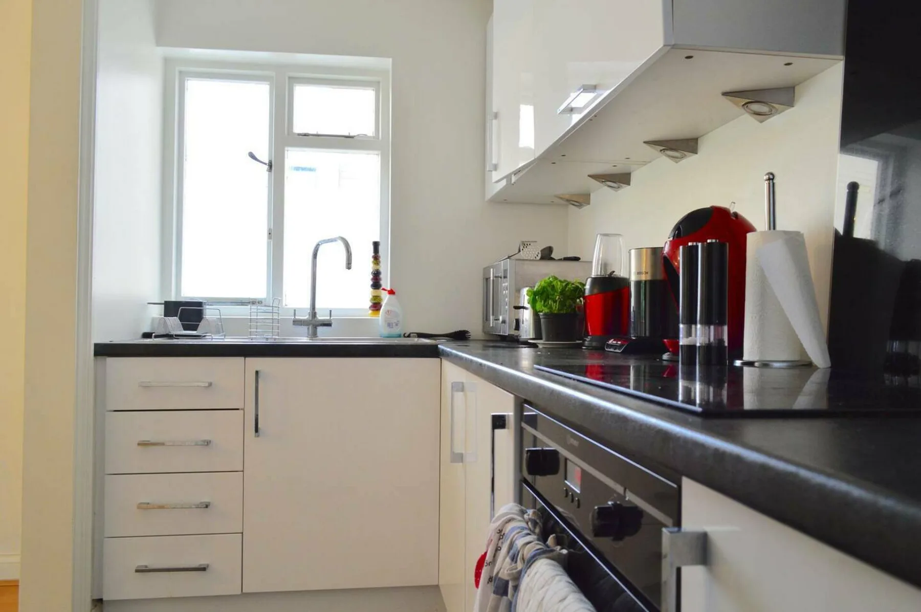 A bright kitchen with white cabinets, dark countertops, and a window above the sink.