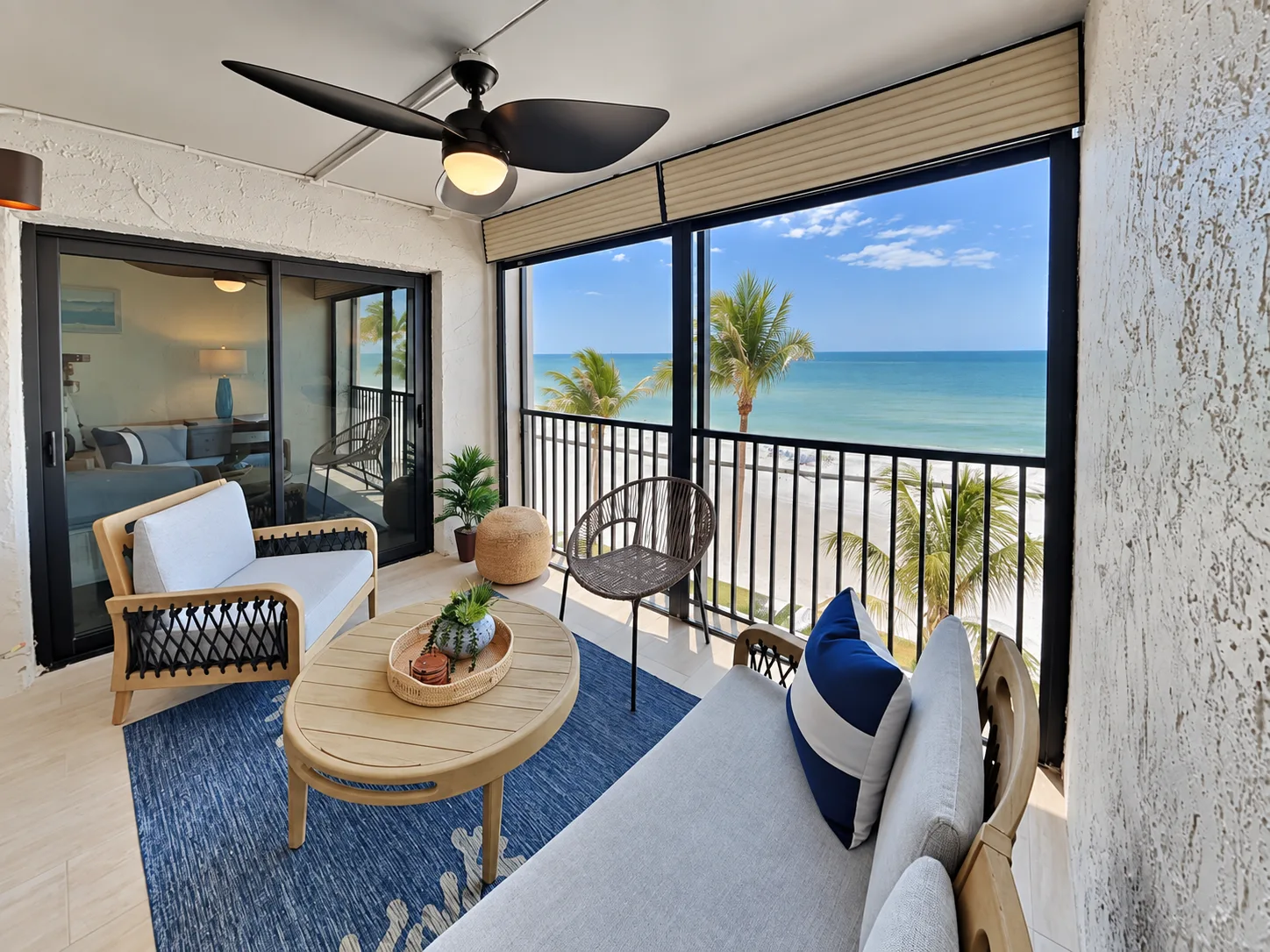 A bright balcony seating area overlooks the ocean through a black railing.