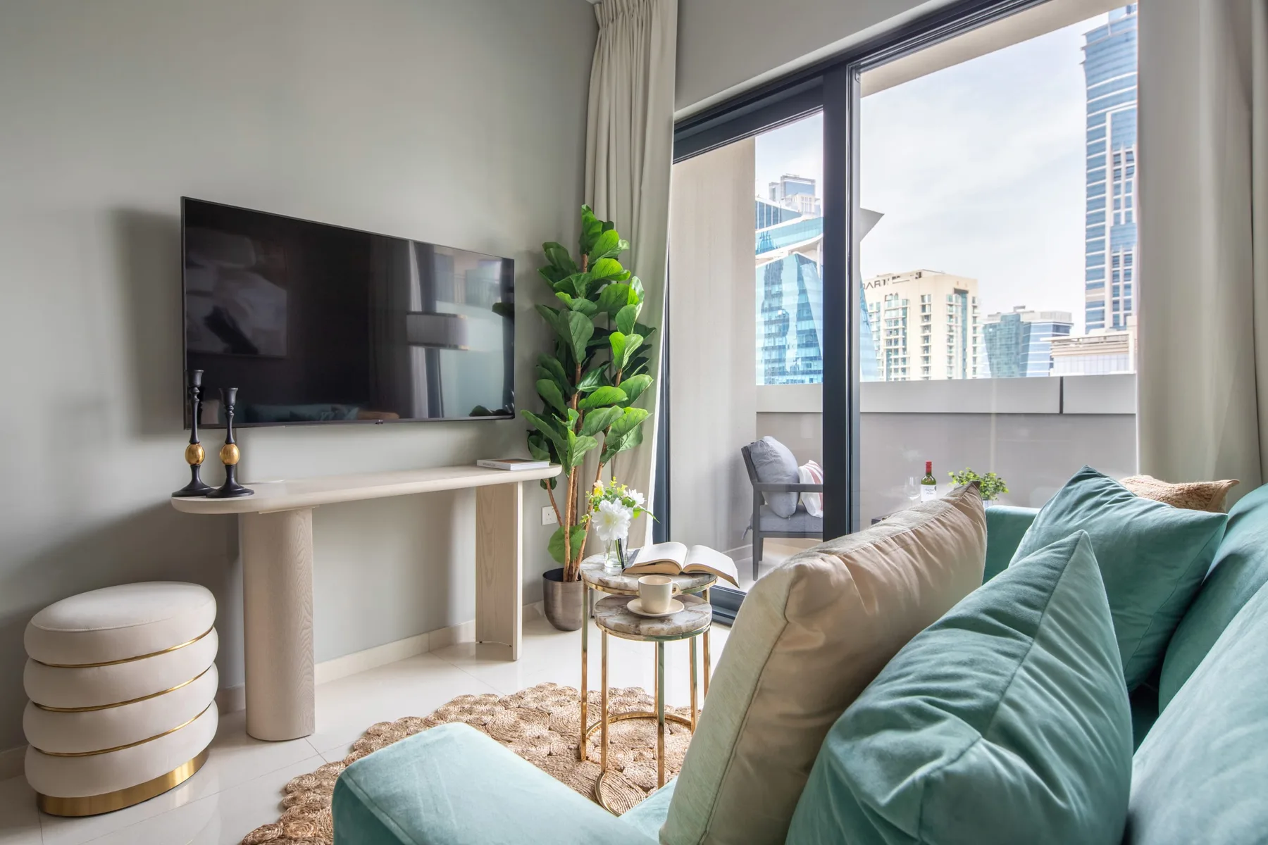 Una sala de estar con asientos, un televisor y grandes ventanales con edificios a la vista.