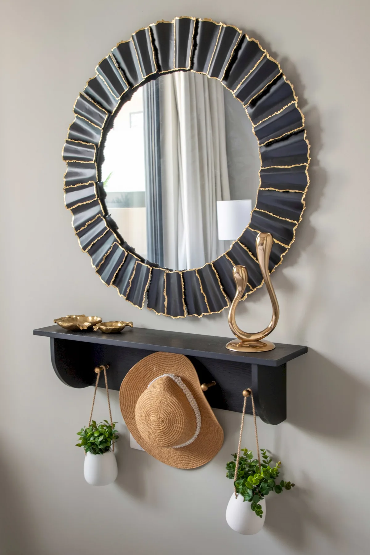 Un espejo decorativo cuelga sobre un estante estrecho con plantas y una lámpara.