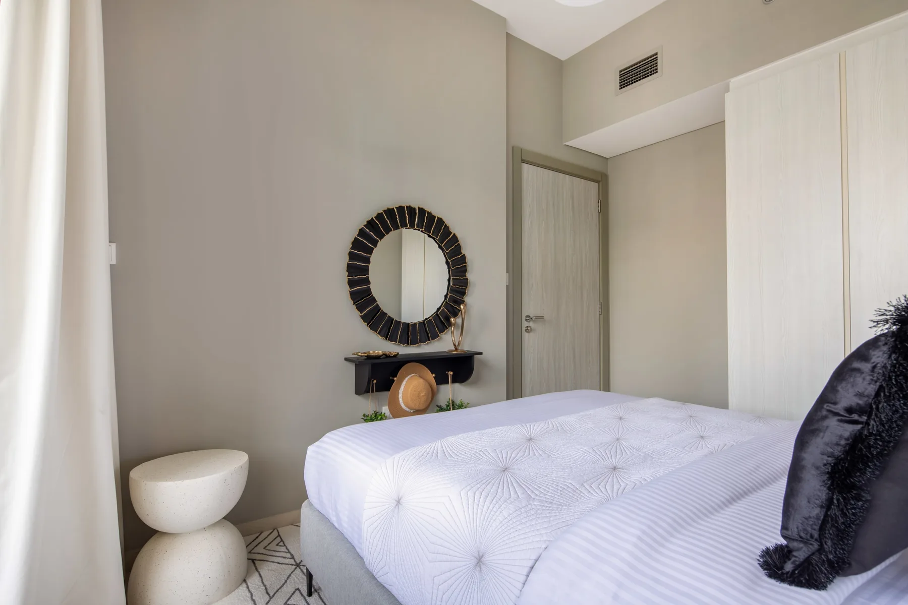 Un dormitorio con una cama, un espejo redondo en la pared y una puerta cerrada.