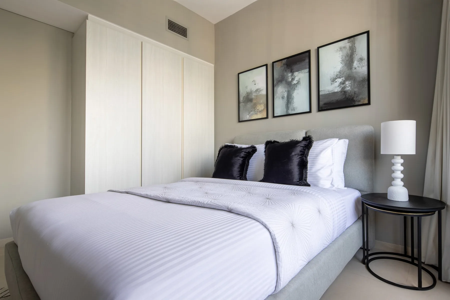 Un dormitorio con una cama bien tendida y cuadros enmarcados sobre el cabecero.