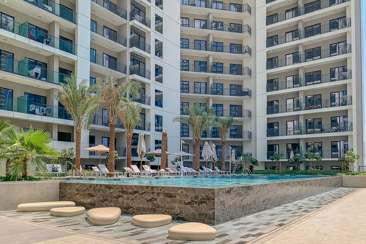 Una piscina en el patio está frente a un edificio de varias plantas con balcones.