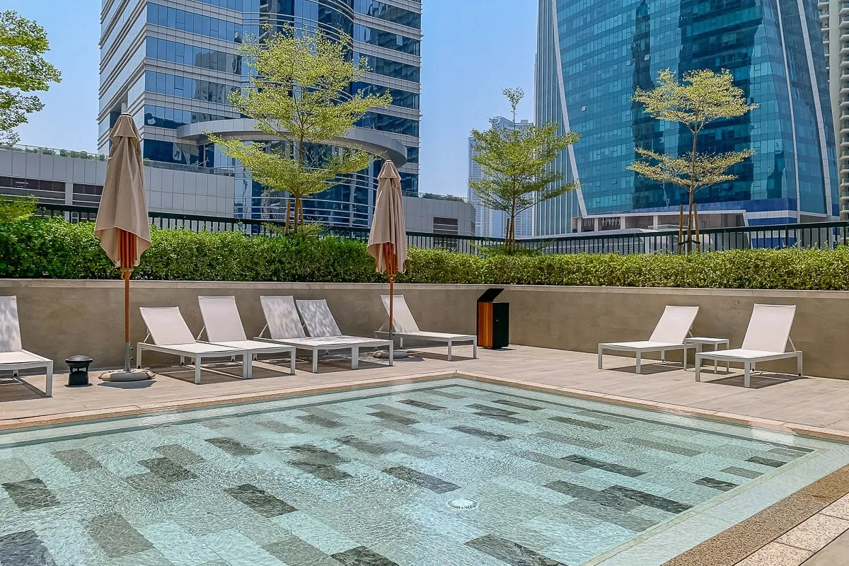 Una piscina al aire libre con asientos y edificios altos de oficinas al fondo.