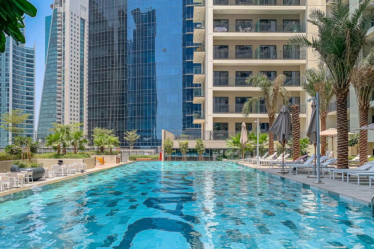 Una piscina al aire libre está rodeada de palmeras y edificios altos.