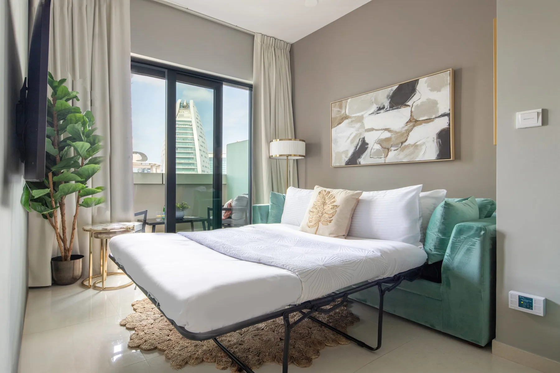 Un dormitorio con una cama grande, asientos verde azulado y puertas de vidrio a un balcón.