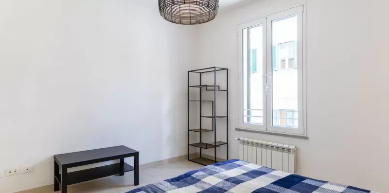 Un dormitorio luminoso con una cama, un banco y una estantería abierta alta.