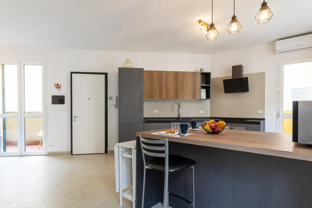 Una cocina-comedor luminosa y diáfana con una isla grande y lámparas colgantes.