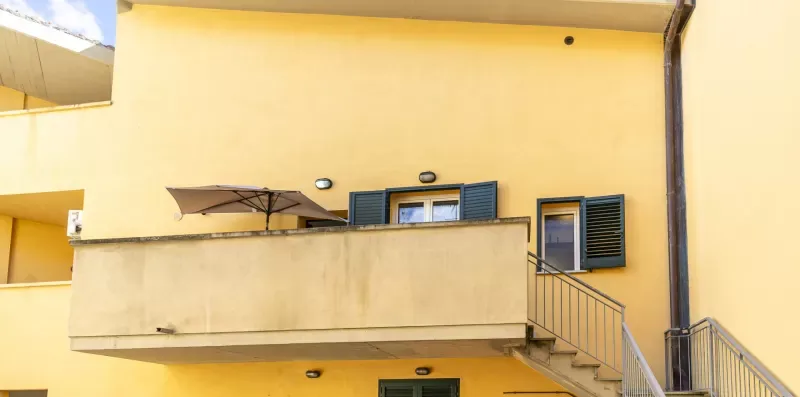 Exterior de un edificio amarillo con un balcón y escaleras exteriores.