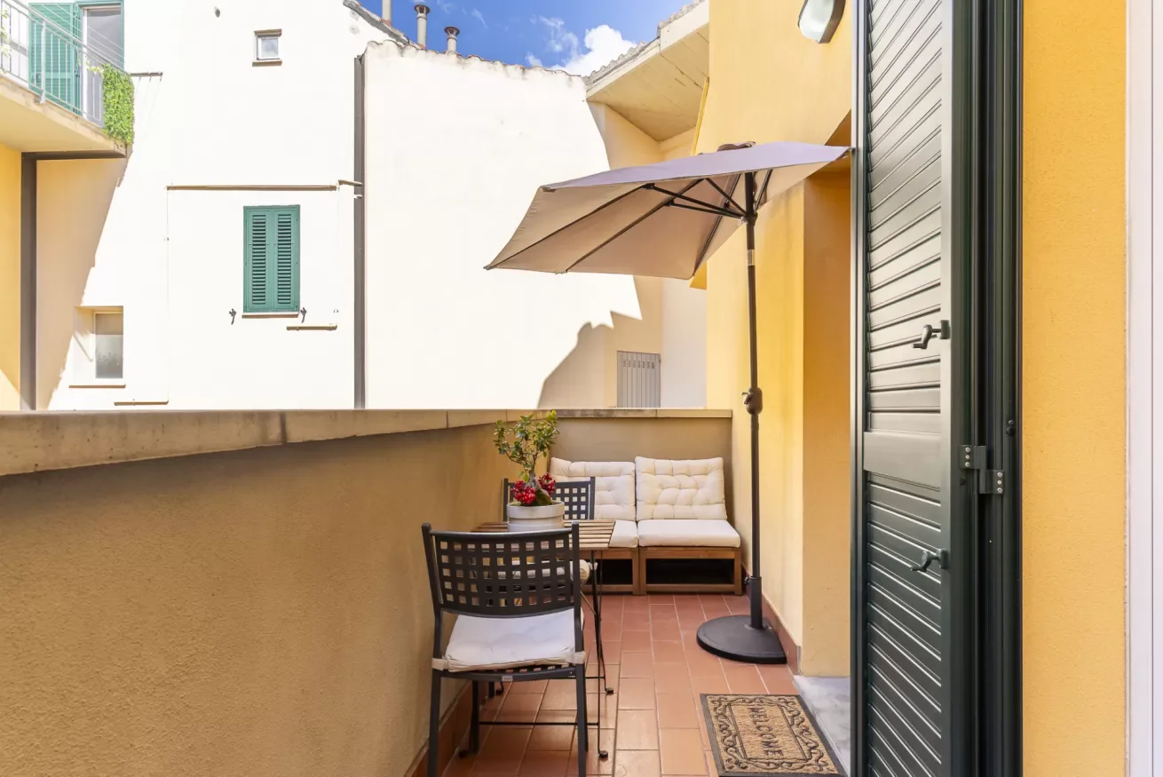 Una pequeña terraza exterior con asientos y una sombrilla grande.