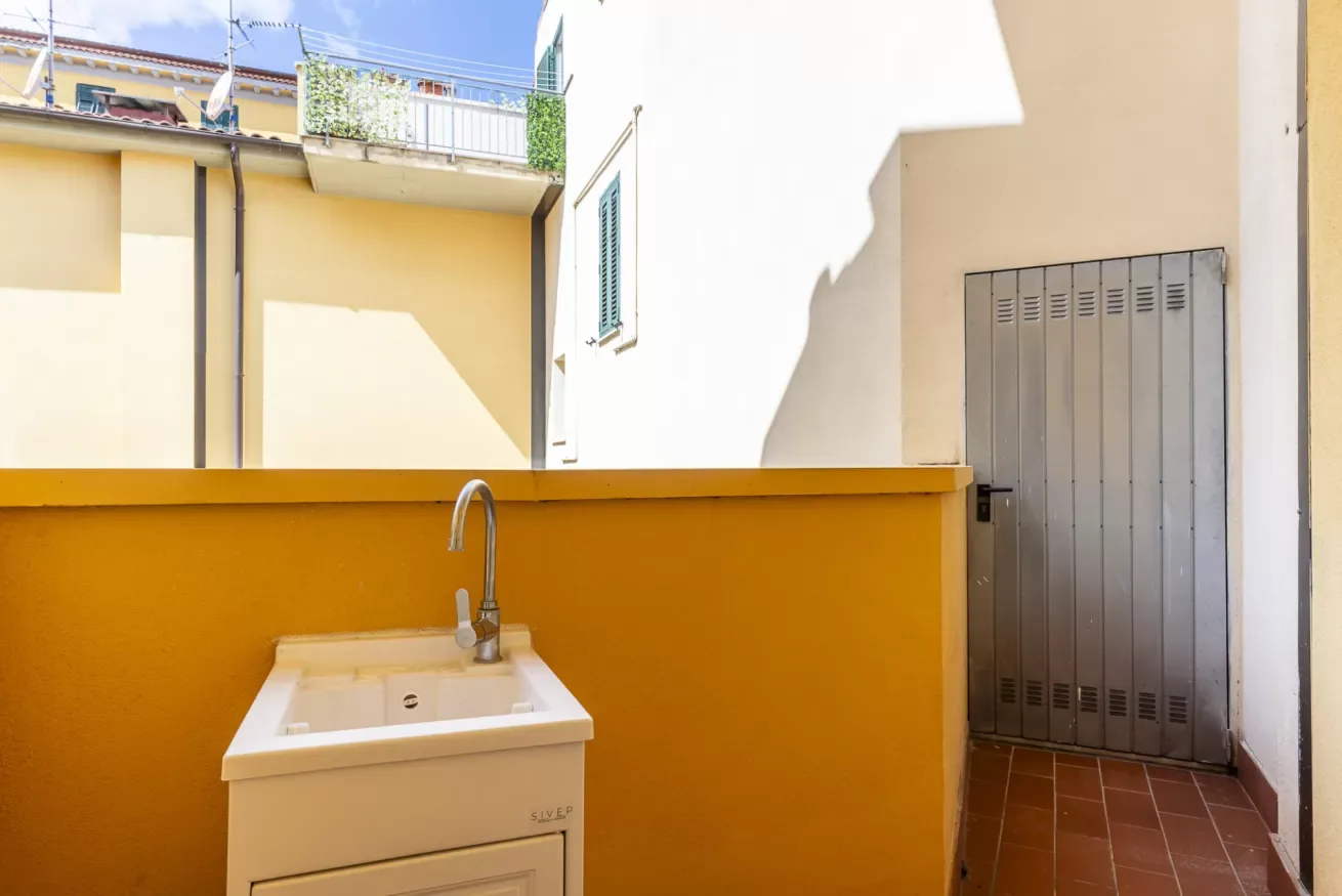 Una pequeña zona exterior de lavado con un lavabo junto a un paso embaldosado.