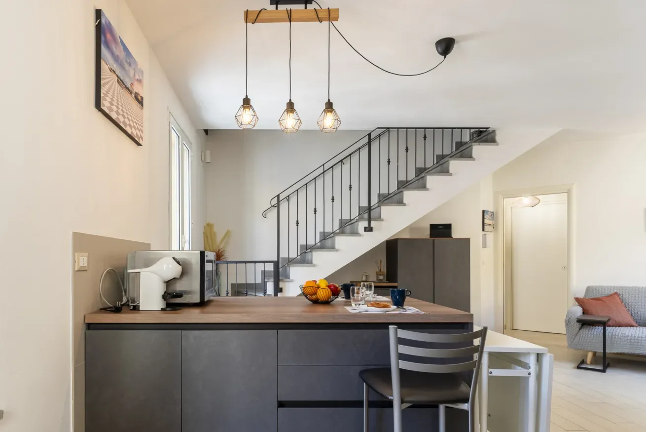 Una isla de cocina con asientos da a una escalera y una zona de estar.