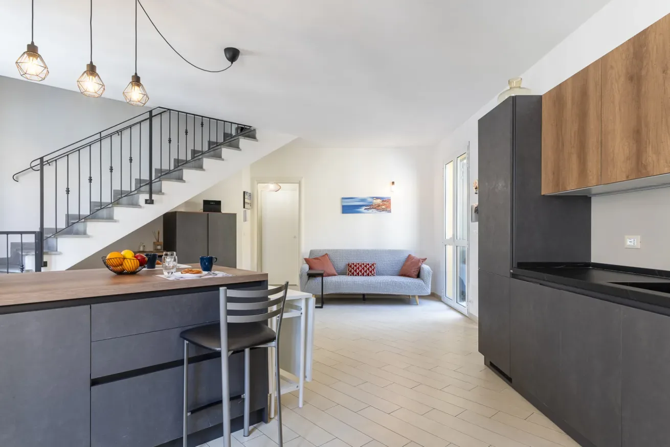 Sala de estar de planta abierta con isla de cocina, asientos de comedor y un sofá bajo la escalera.