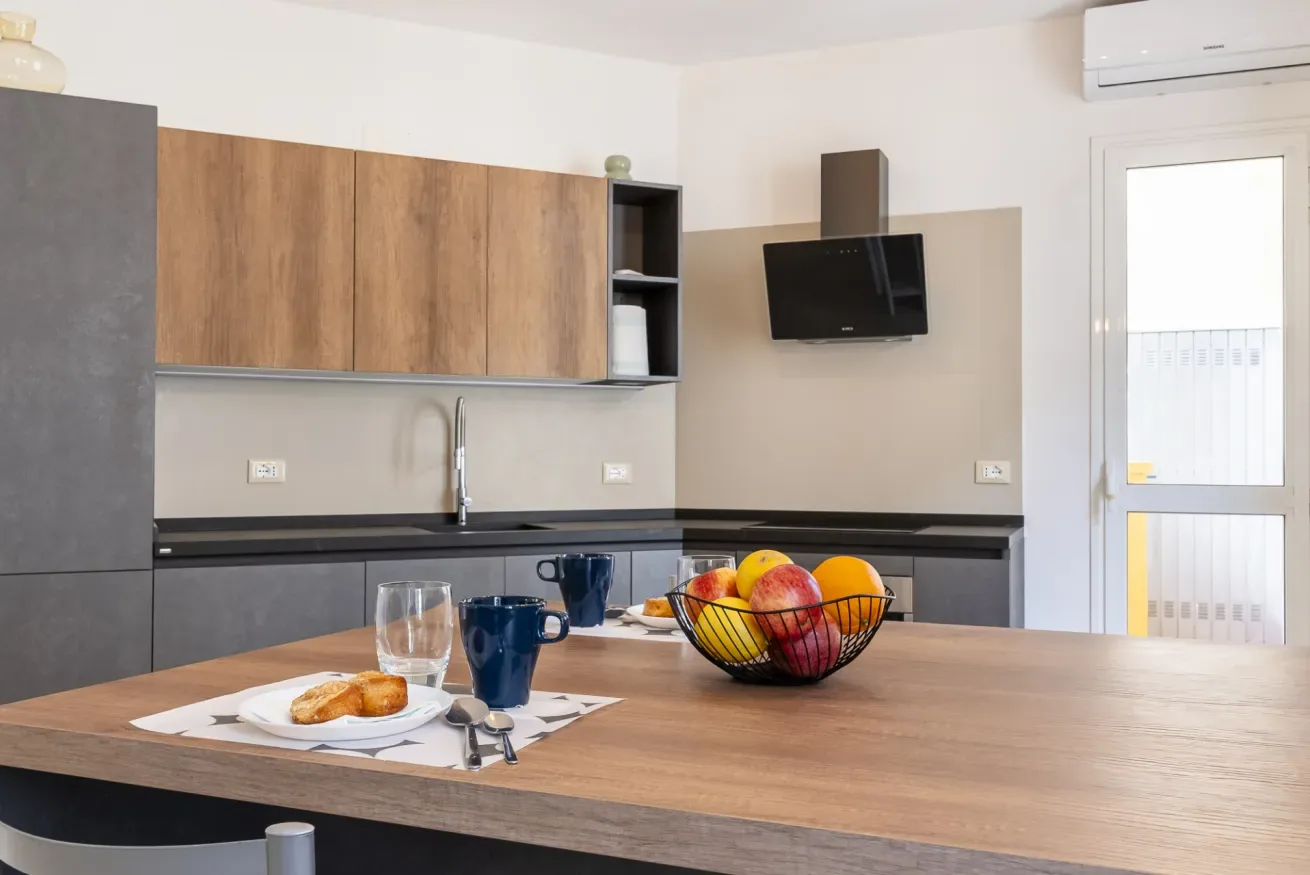 Una cocina moderna con gabinetes de madera, encimera oscura y un frutero sobre la isla.