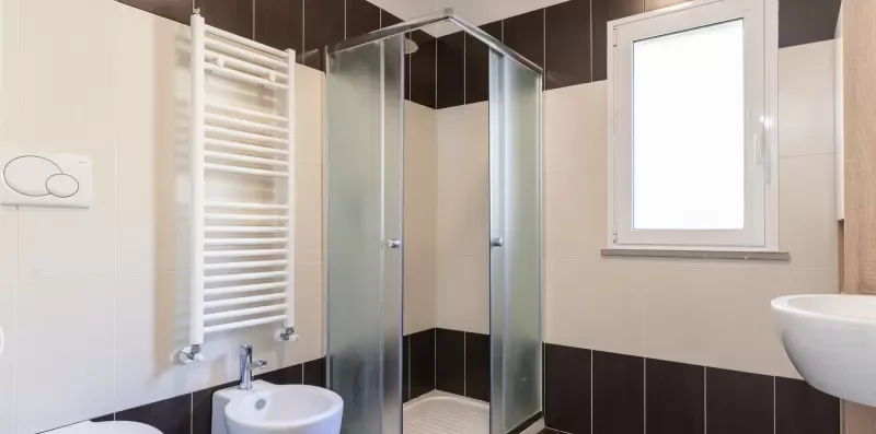 A tiled bathroom with a glass shower and a window.