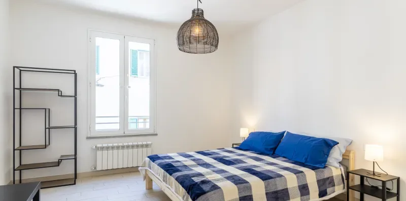 A bedroom with a bed covered in blue and white checks beside a window.
