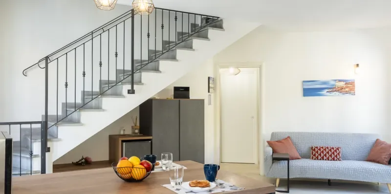 Una sala luminosa con sofá, mesa de comedor y escalera.