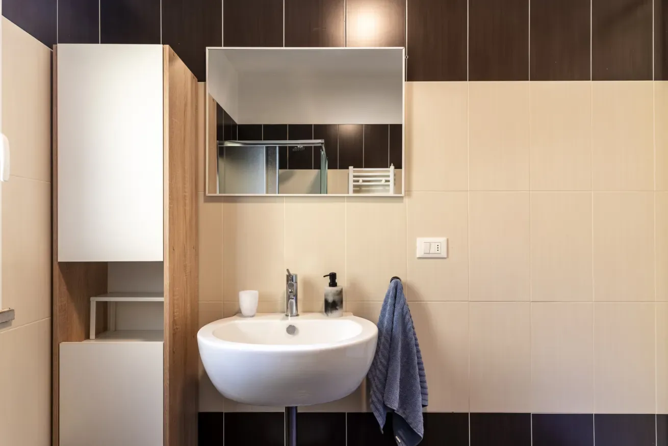 Un tocador de baño con lavabo blanco, espejo de pared y una toalla colgada.