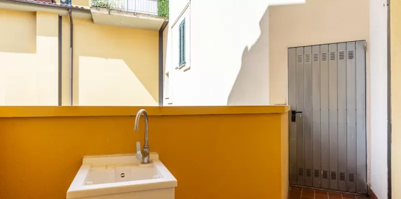 Una pequeña zona de lavado al aire libre con un lavabo junto a una puerta metálica alta.