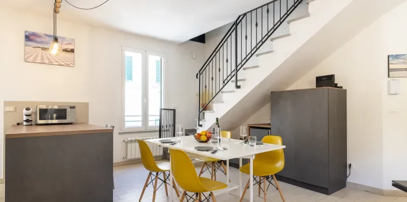 A bright kitchen and dining area with a table and yellow seating beneath a staircase.