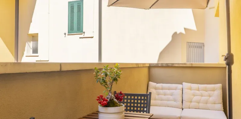 Una zona de estar al aire libre tiene asientos acolchados, una mesa pequeña y una planta en maceta.