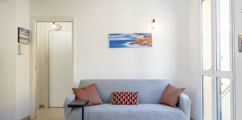 Una sala de estar con un sofá gris, cojines decorativos y una imagen costera en la pared.
