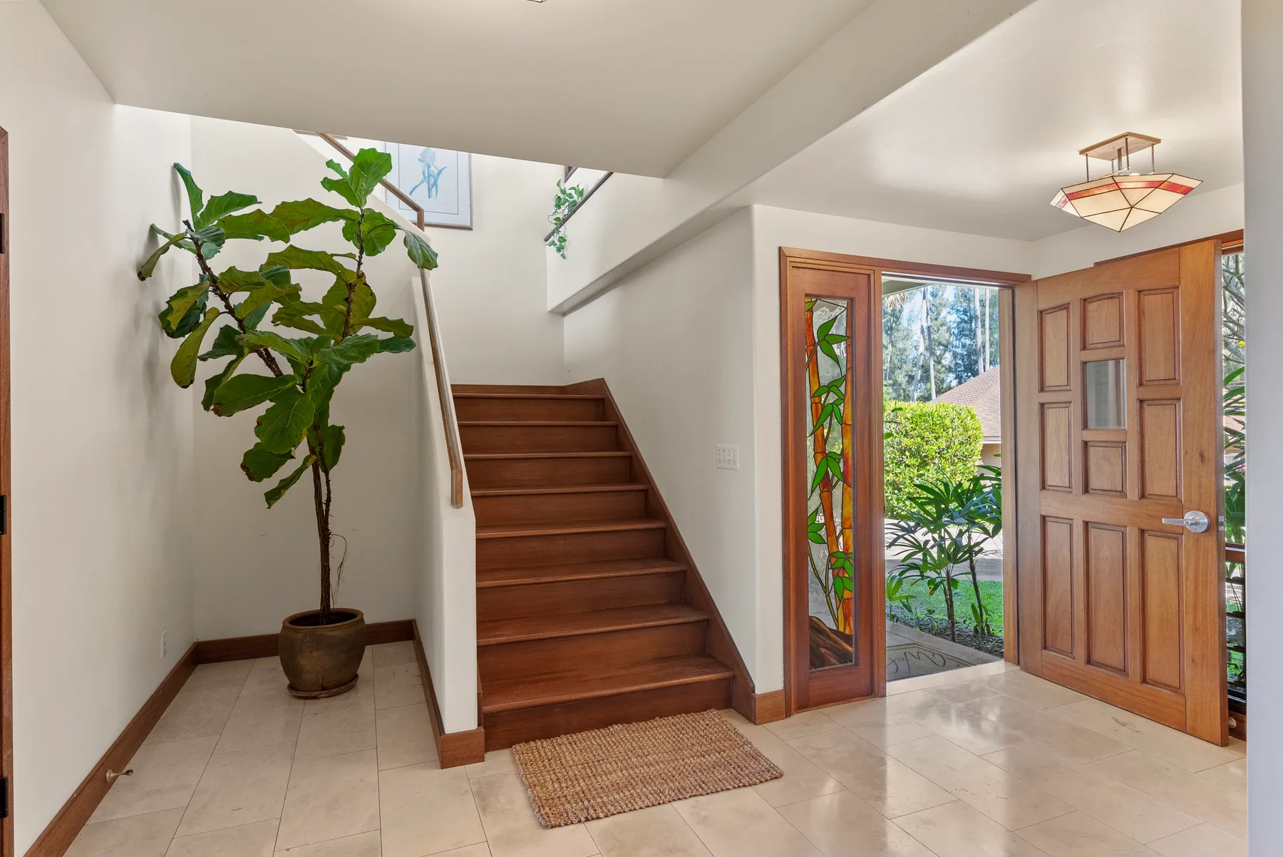 Una entrada interior con una escalera de madera, la puerta principal abierta y una planta en maceta.