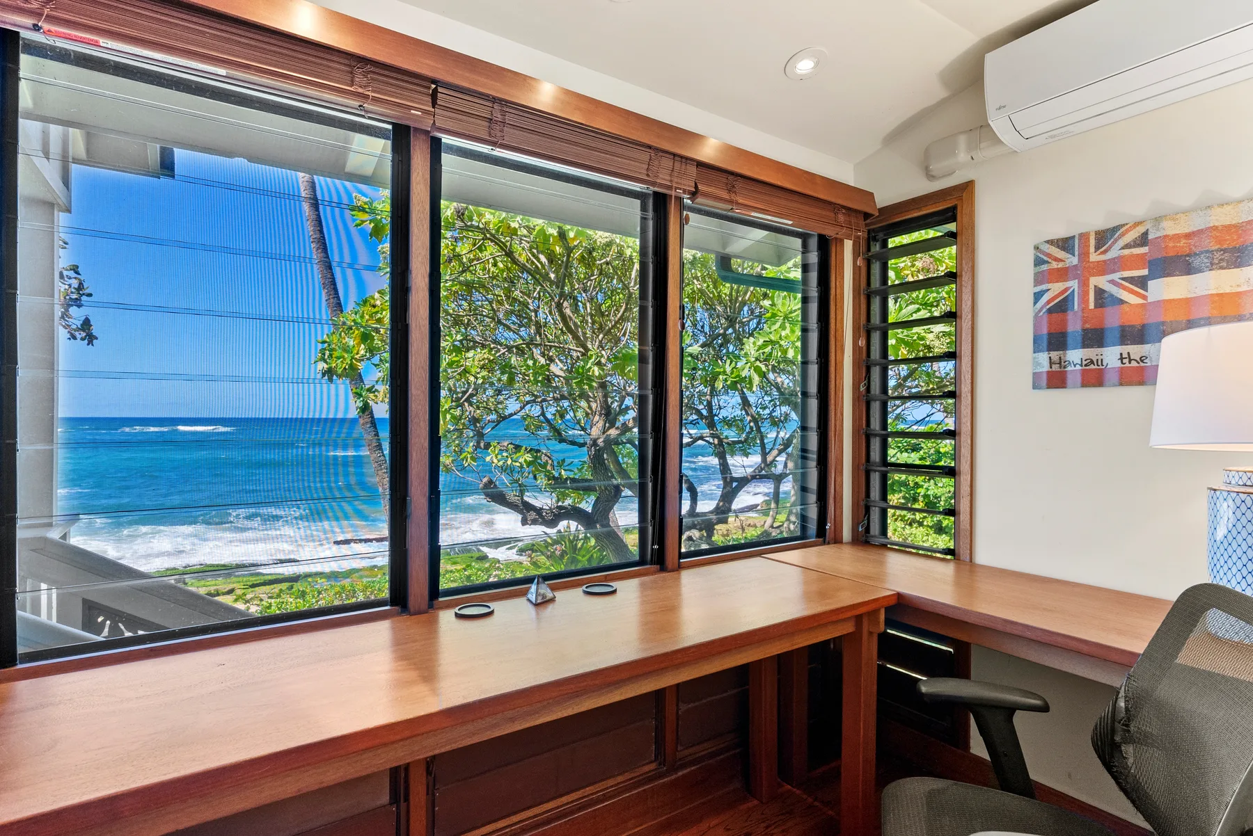 Un espacio de trabajo con escritorio mira por grandes ventanas al océano y a árboles frondosos.
