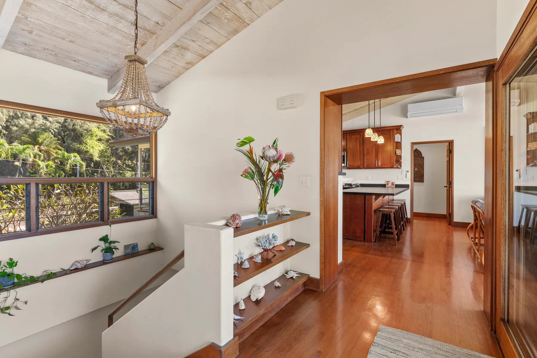 Un pasillo interior luminoso con una repisa de madera y una puerta abierta hacia la cocina.
