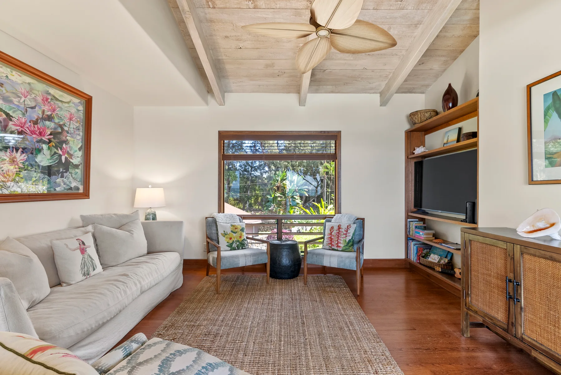 Una sala luminosa con asientos, un televisor y una gran ventana con vegetación al otro lado.