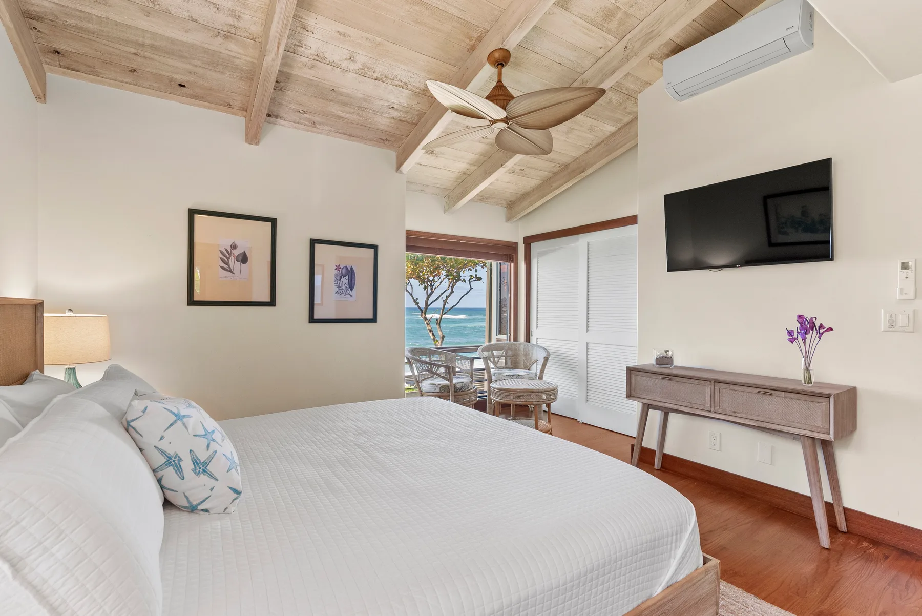 Un dormitorio luminoso con una cama, un televisor en la pared y puertas que dan a un pequeño patio.