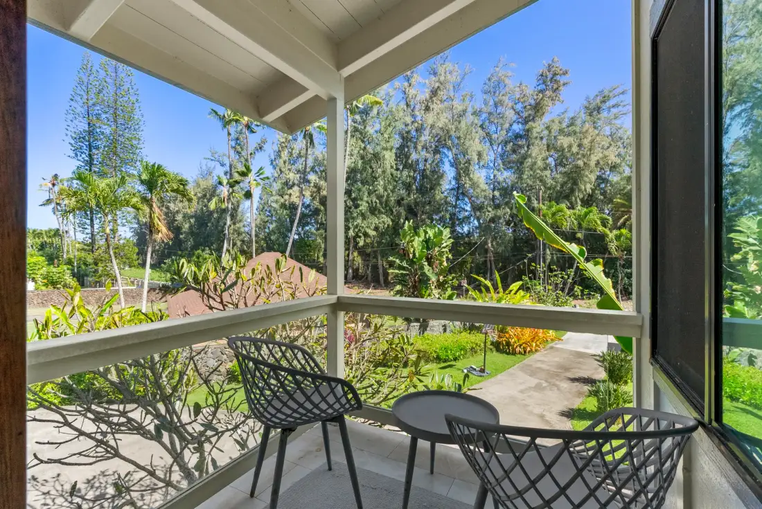 Un patio cubierto da a un jardín, con asientos de metal junto a la barandilla.