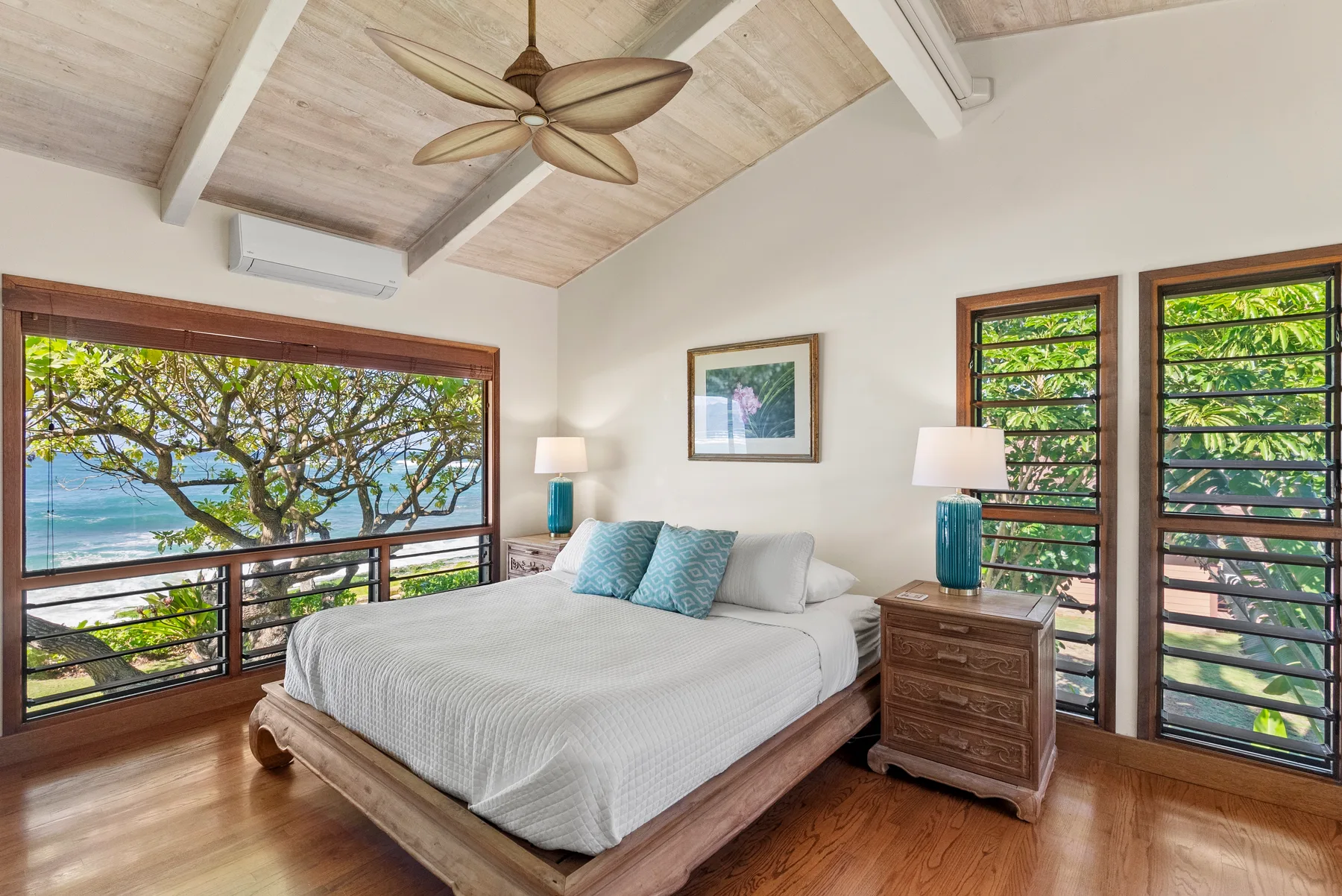 Un dormitorio luminoso con una cama grande junto a ventanas con vistas a árboles y agua.