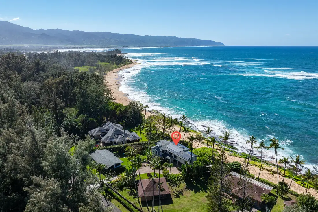 Aerial view of a coastal resort beside a forested shoreline and turquoise ocean.