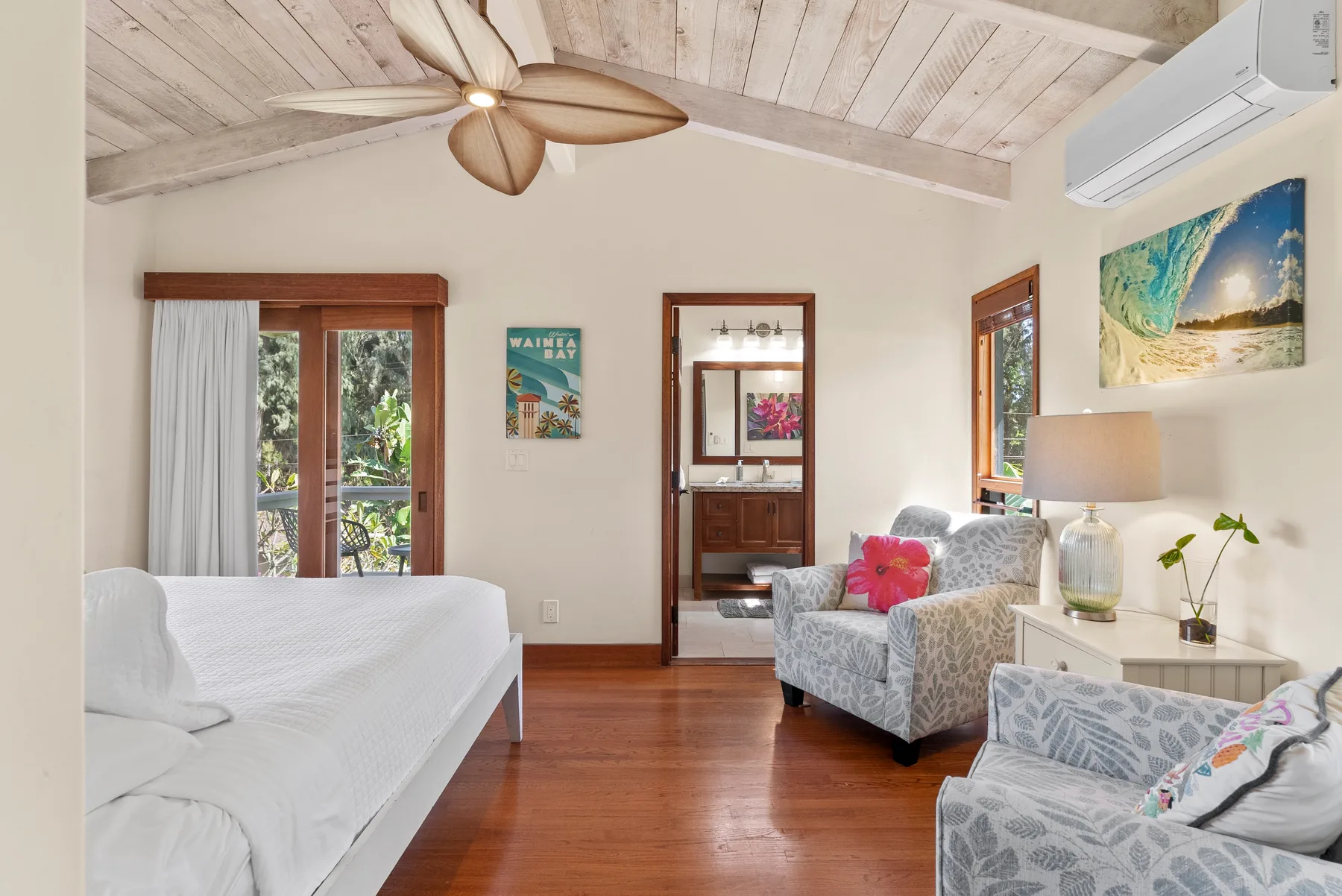 Un dormitorio luminoso con cama, asientos y ventilador de techo bajo un techo inclinado de madera.