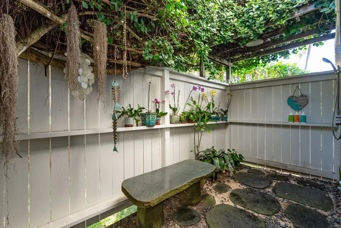 Un rincón de jardín al aire libre con plantas en macetas junto a una cerca blanca.