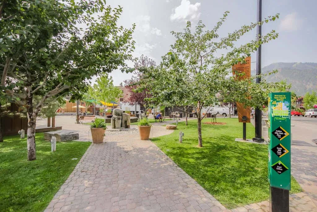 A paved garden walkway winds between green lawns and leafy trees.
