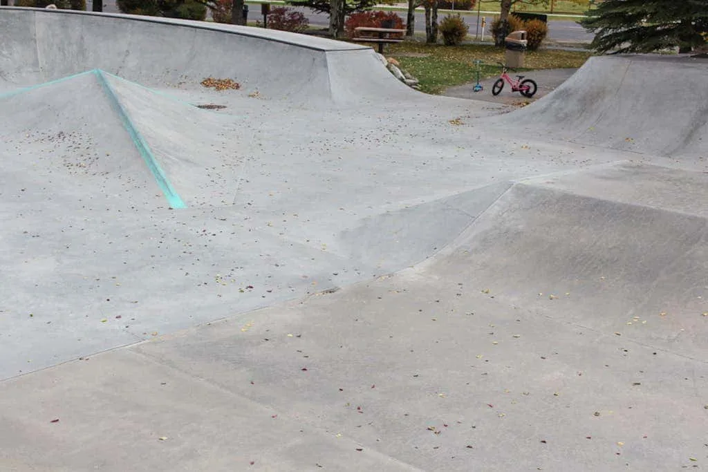 A concrete skatepark bowl with curved ramps and a small bicycle nearby.