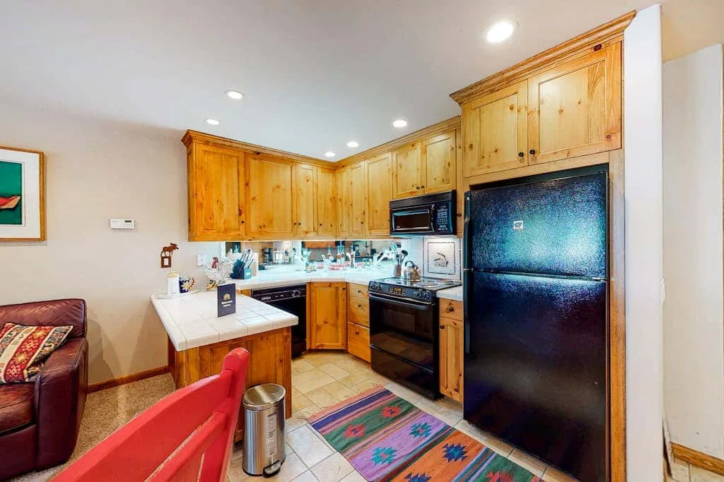 A kitchen with wooden cabinets, dark appliances, and a tiled floor.
