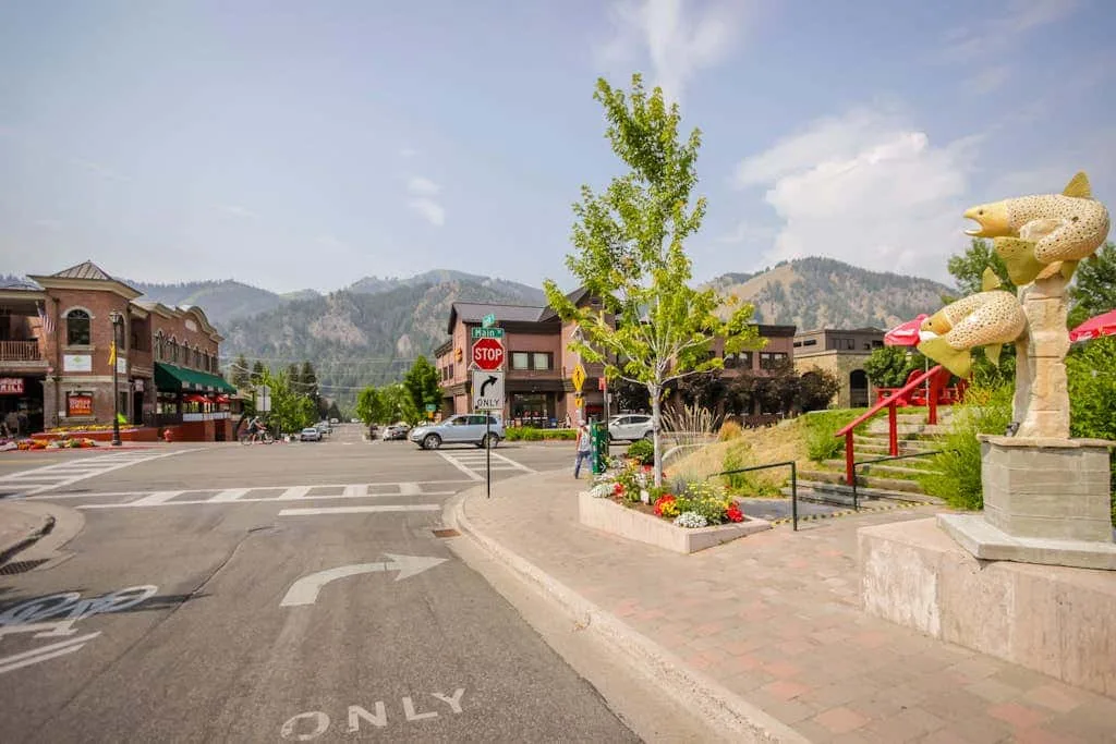 A small-town street intersection beside a landscaped sidewalk and public sculptures.