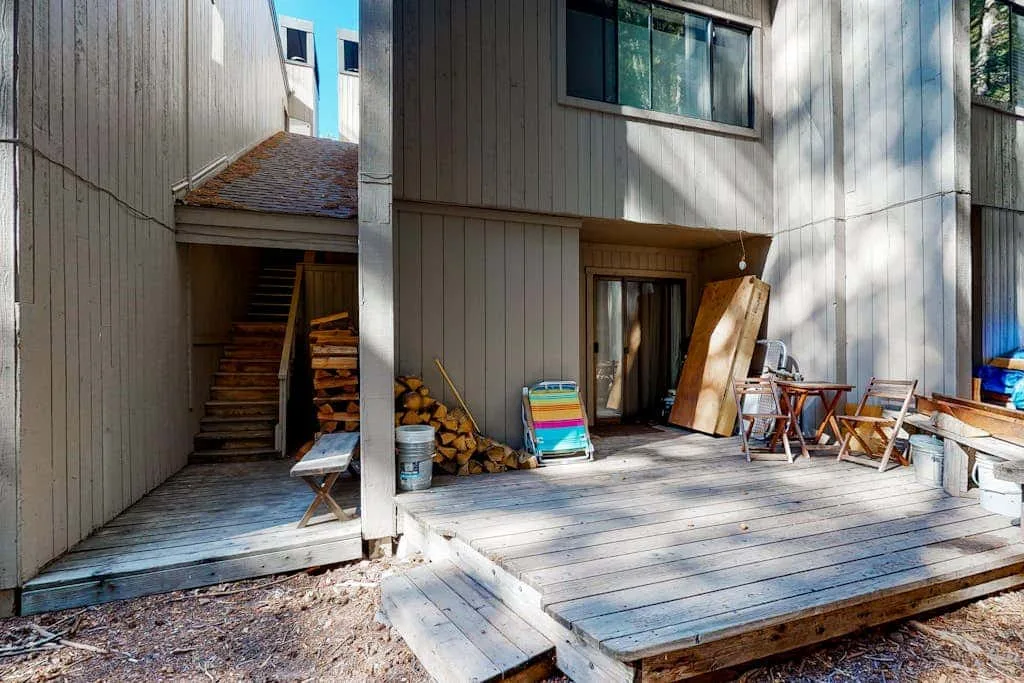 A wooden deck beside a paneled building, with outdoor seating and a stairway.