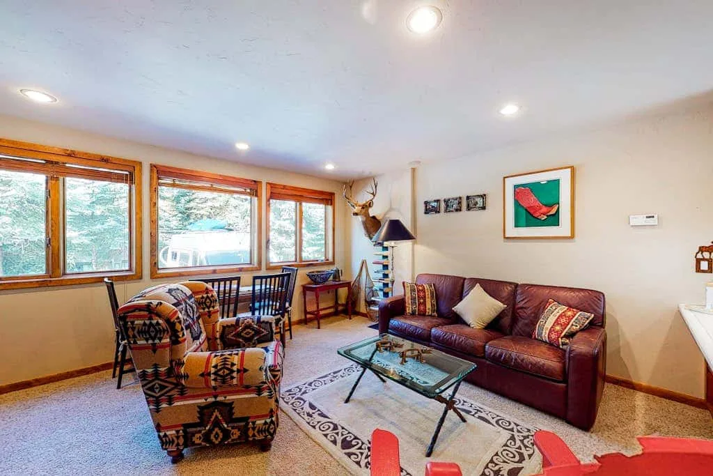 A living room with seating around a glass coffee table and large windows.
