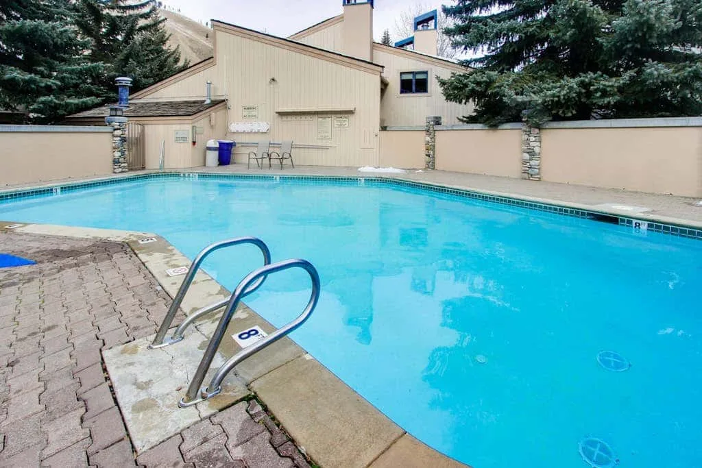 An outdoor swimming pool sits beside a paved deck and a beige building.