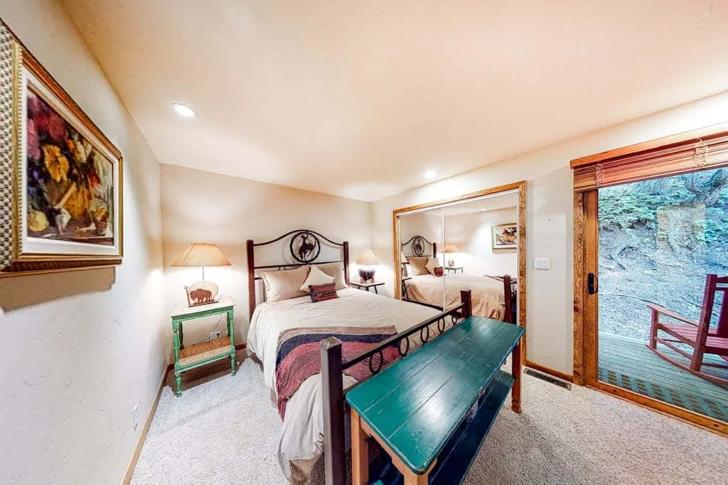 A bedroom with a bed, a green bench, and a large mirror.