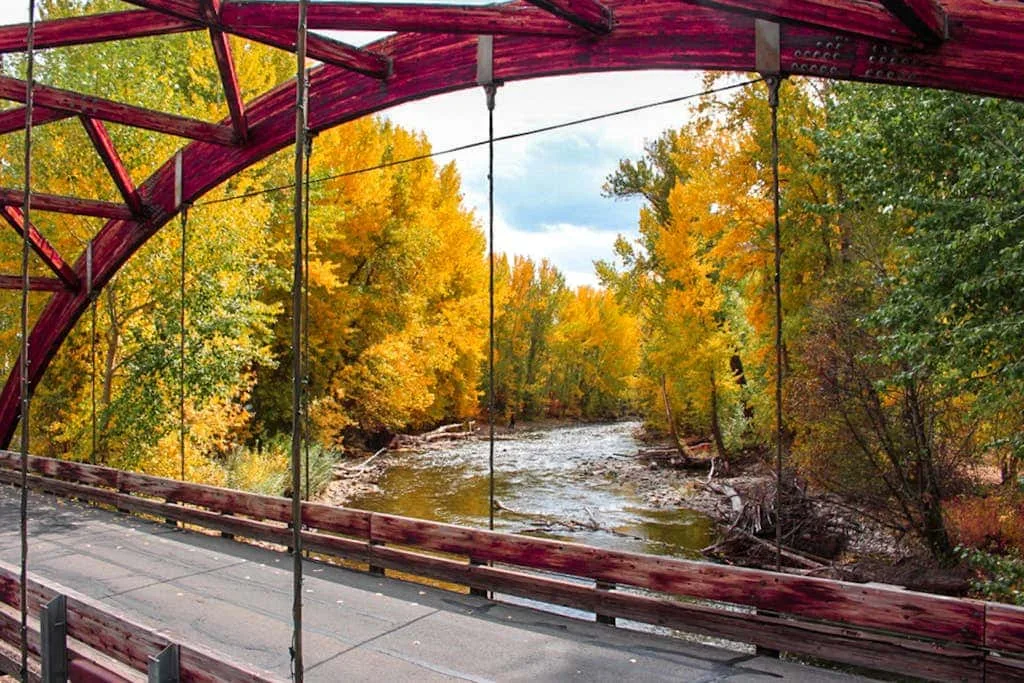 A red bridge spans a river surrounded by colorful autumn trees.