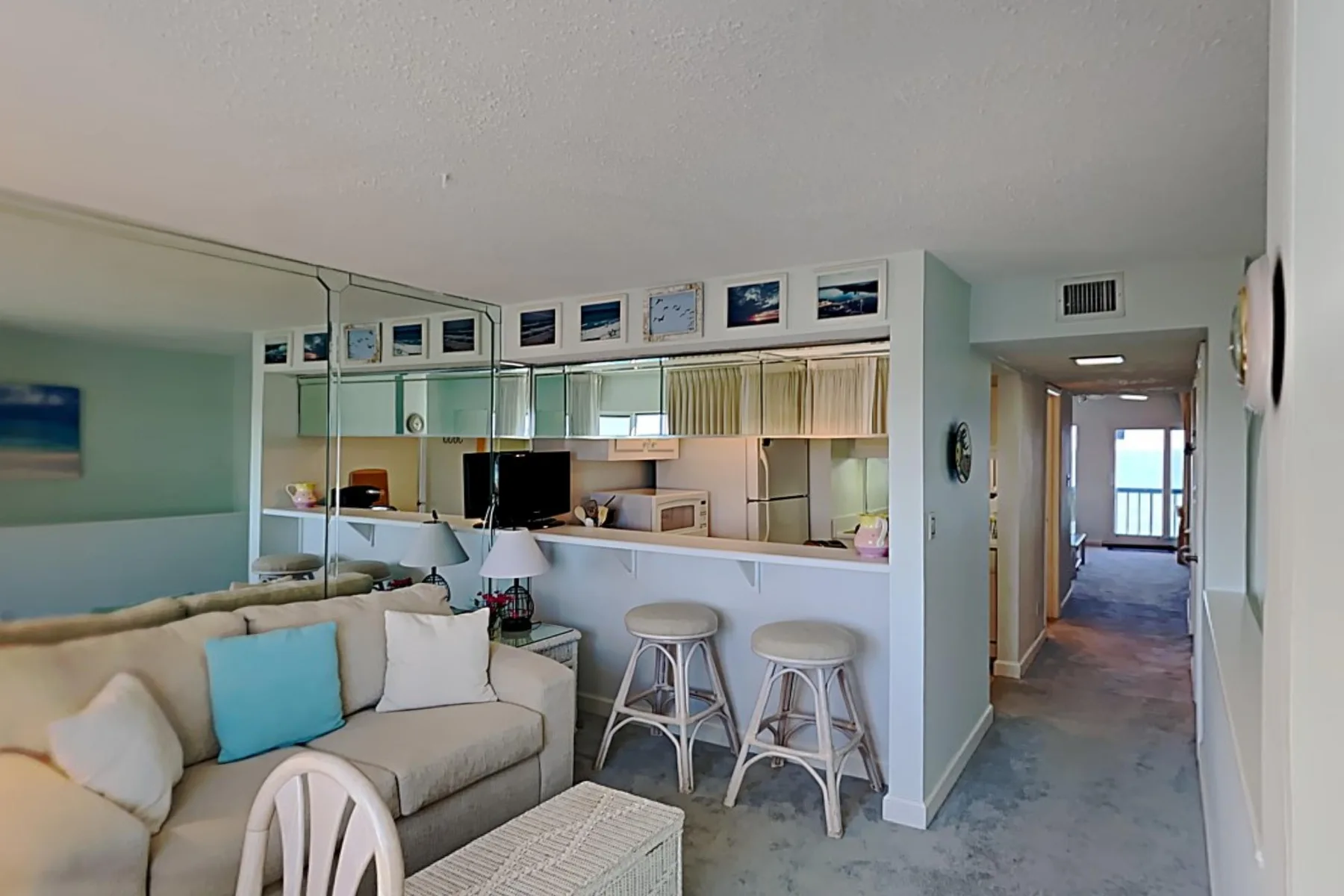 A living area with a sectional sofa, bar stools, and a hallway leading toward a window.