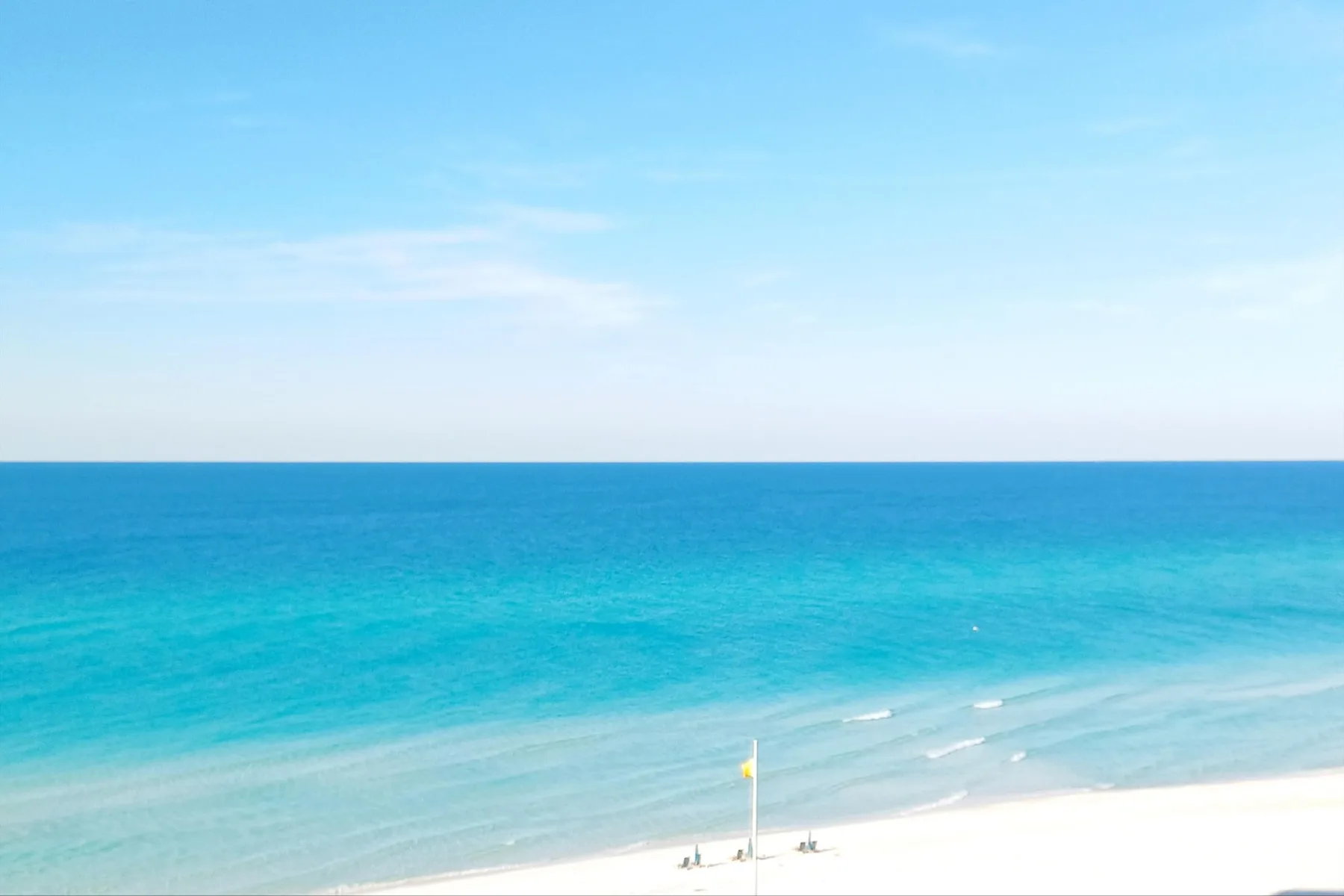 A broad view of turquoise sea and pale sand beneath a clear sky.
